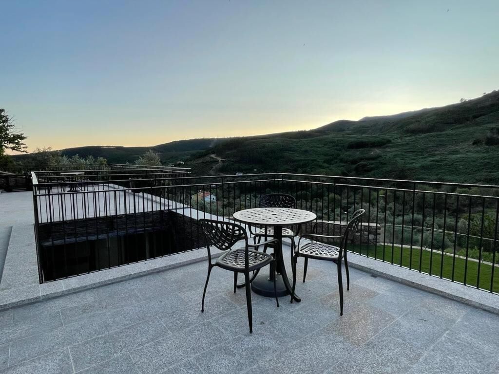 A terrace with a round table and four chairs, surrounded by a black metal railing.