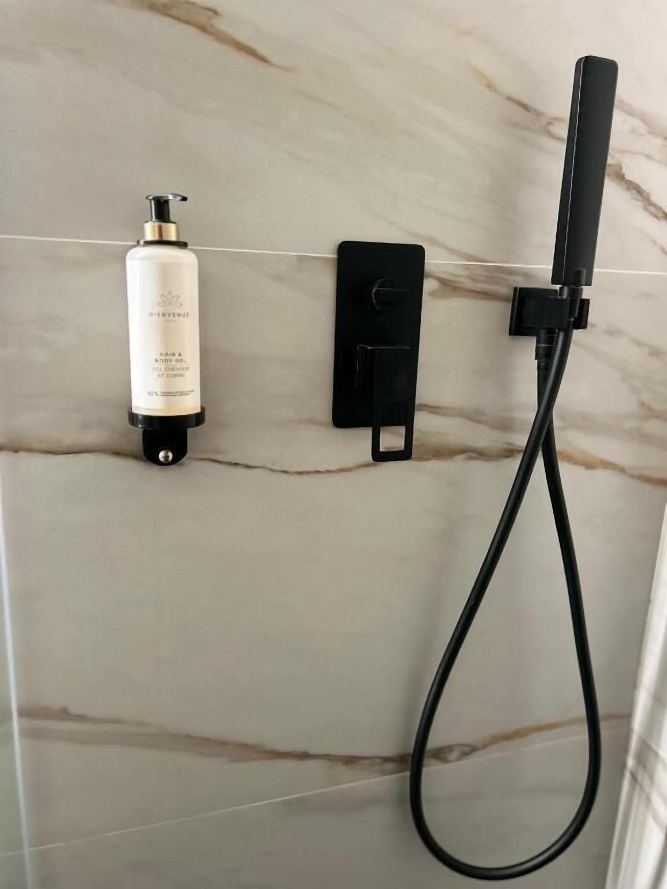 A bathroom with a marble wall, a bottle of shampoo, a black soap dispenser, and a handheld showerhead.