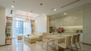 A modern living room with a white sofa, a dining table with chairs, and a chandelier.