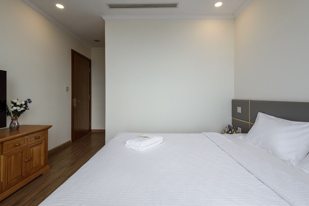 Een hotelkamer met een opgemaakt bed, een houten dressoir en een televisie aan de linkerkant.