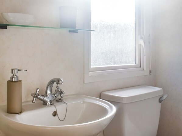Un baño con lavamanos blanco, inodoro y ventana.