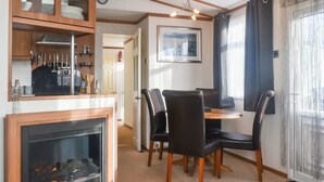 Een eetgedeelte met een tafel en stoelen, een open haard, en een keuken met kasten en keukengerei.