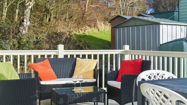 Een terras met tuinmeubilair, waaronder een bank en stoelen, en een bijzettafeltje met twee wijnglazen.