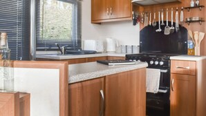 Een kleine keuken met houten kastjes, een fornuis en een raam met zonwering.
