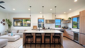 A modern kitchen with a central island, bar stools, and a dining area with a sofa and coffee table. - Modern Kauaʻi Luxury Home With Ohana, Pool, and Spa in Kukuiʻula (Koloa)