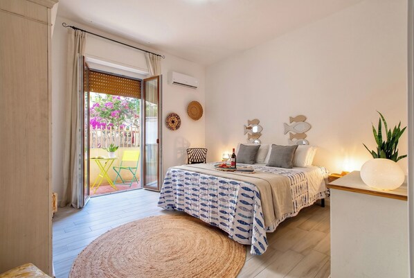 A bedroom with a bed, bedside table, lamp, and a view of the outside.