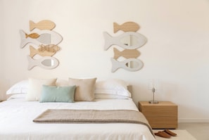 A bedroom with a bed, pillows, a bedside table with a lamp, and wall art.