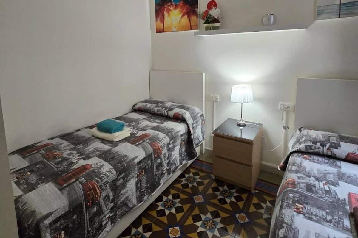 A room with two beds, a nightstand, a lamp, and a ceiling light.