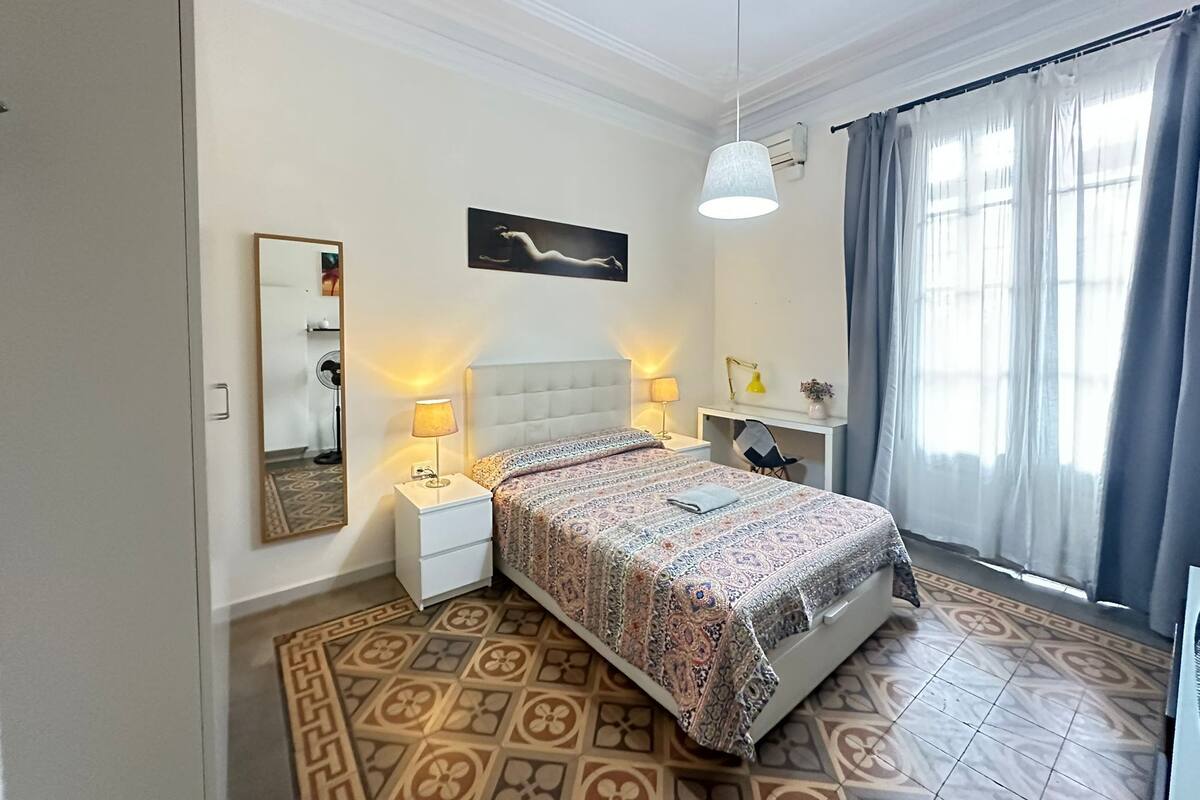 A bedroom with a bed, nightstands, a desk, and a chair.