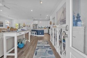 Une cuisine moderne avec des meubles blancs, un îlot central et un coin repas comprenant une table et des chaises blanches.