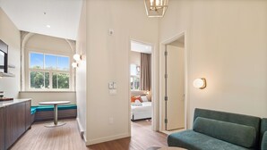 A modern hotel room with a dining area, a sofa, a small round table, and a view of the outdoors through a large window. - Arcadia Hotel Boutique (Montréal)
