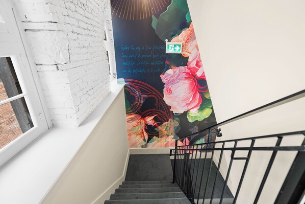 A staircase with a black railing, a white brick wall, and a mural with floral designs. - Arcadia Hotel Boutique (Montréal)