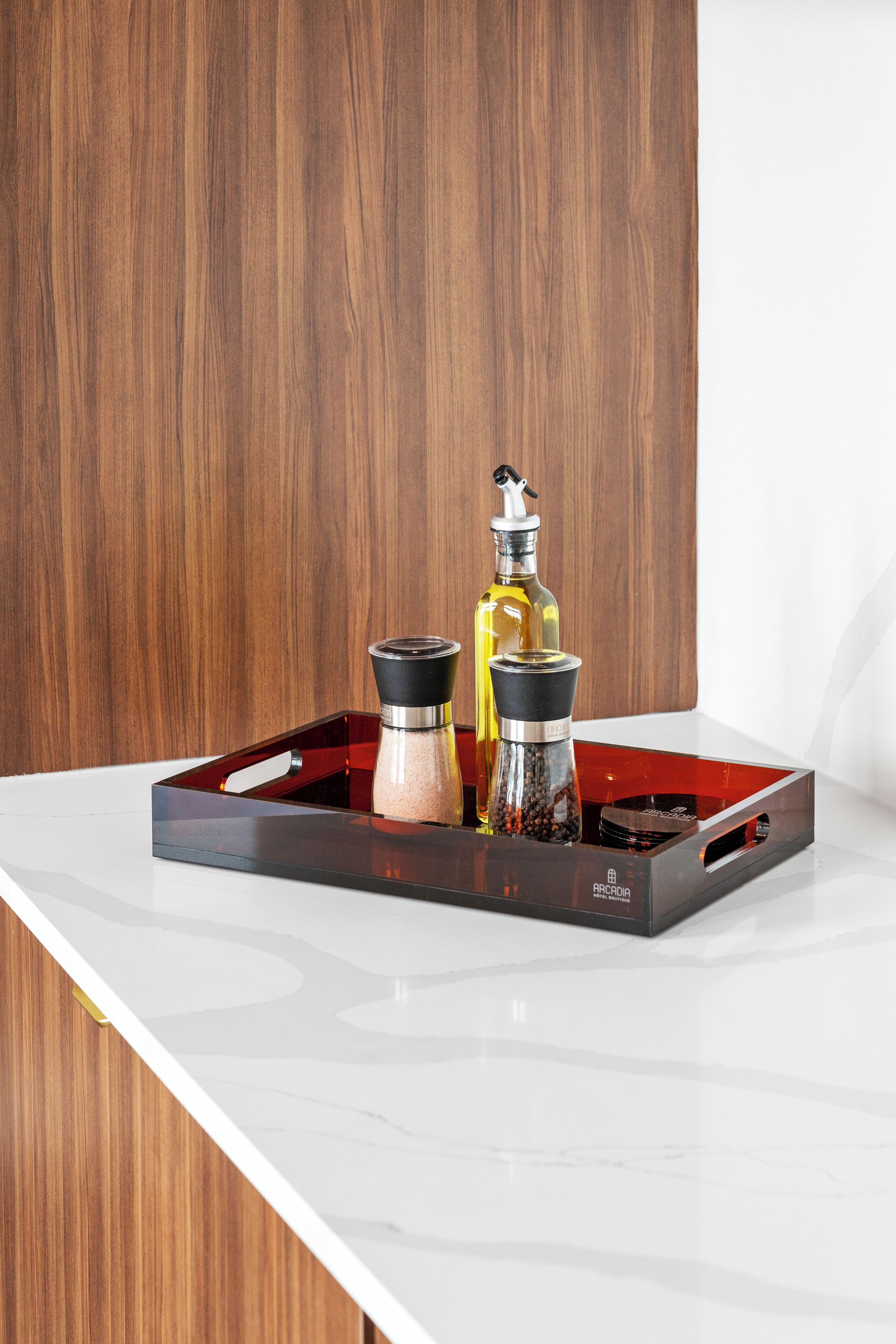 A kitchen counter with a marble top, a wooden wall in the background, and a black tray holding pepper and salt shakers.