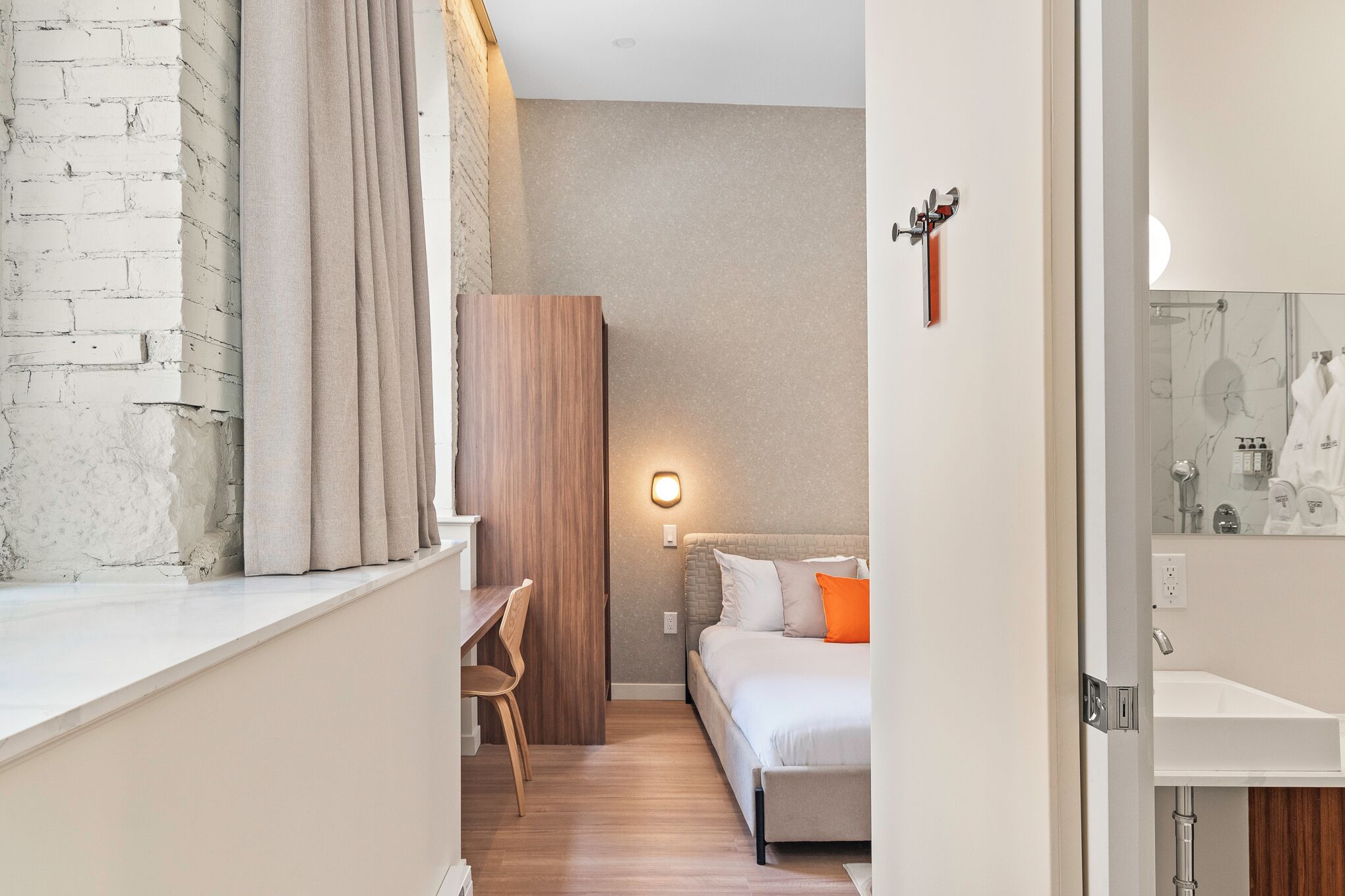 Una habitació d'hotel moderna amb un escriptori de fusta, un llit amb almoades taronges i un bany amb un lavabo de marbre.