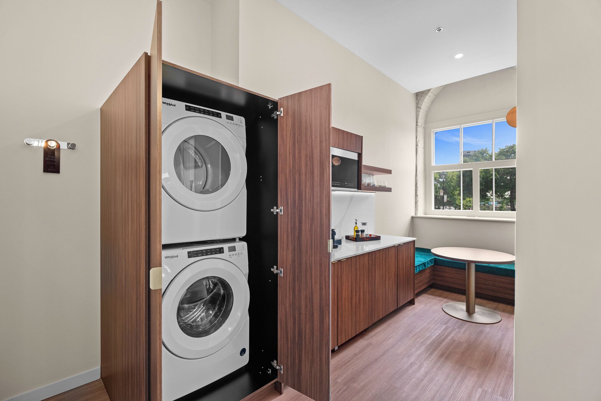 A compact laundry room with two stacked washers and dryers, a small kitchenette, and a window providing natural light.