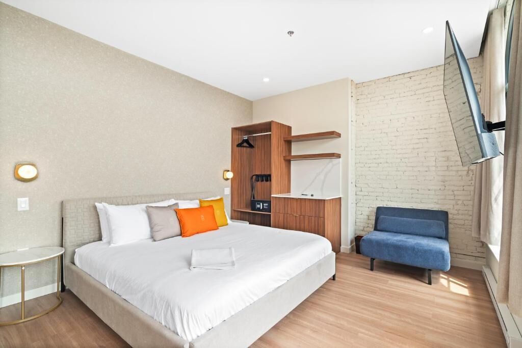 Quarto de hotel moderno com uma cama grande, uma escrivaninha, uma cadeira e uma televisão na parede.