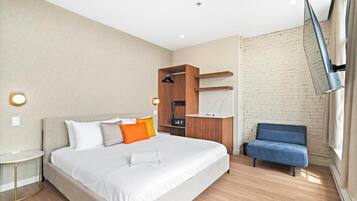 Quarto de hotel moderno com uma cama grande, uma escrivaninha, uma cadeira e uma televisão na parede.