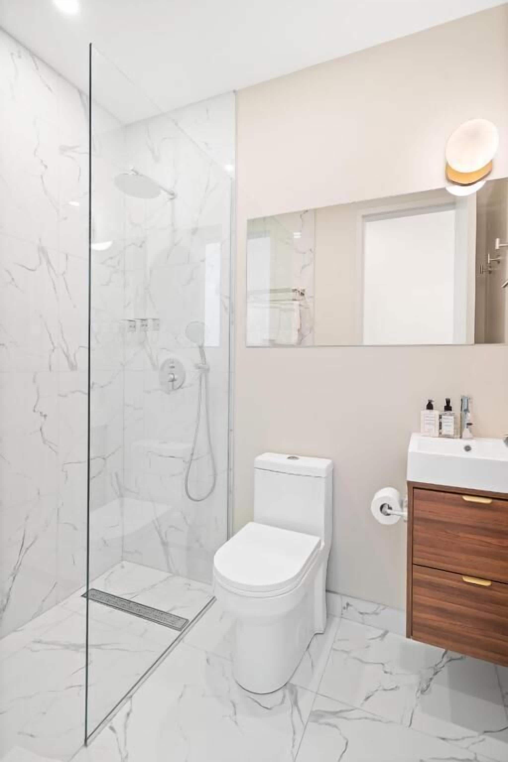 Un baño moderno con cabina de ducha de vidrio, inodoro, tocador con espejo y suelo de mármol.
