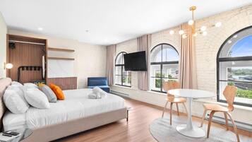 Een moderne hotelkamer met een bed, een televisie, een zithoek met stoelen en grote ramen met uitzicht op de stad.