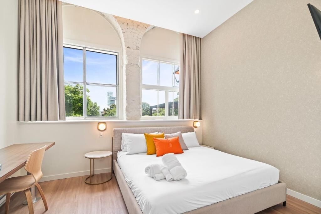 A bedroom with a large bed, a desk, and a window with curtains.