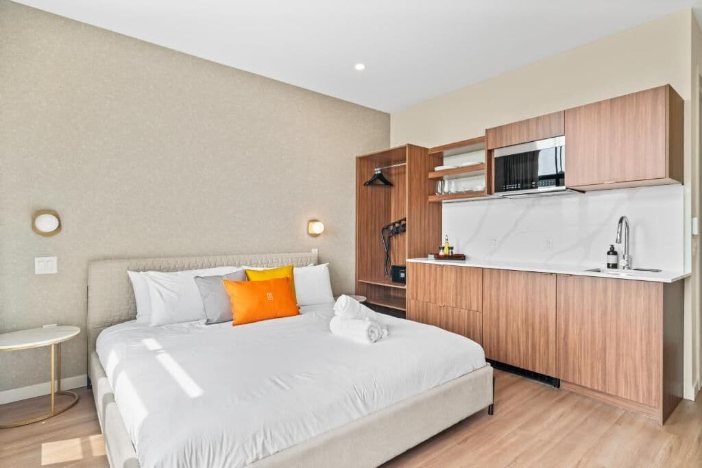 Una habitación de hotel moderna con una cama grande, una cocina integrada con microondas y fregadero, y una pequeña mesa redonda.