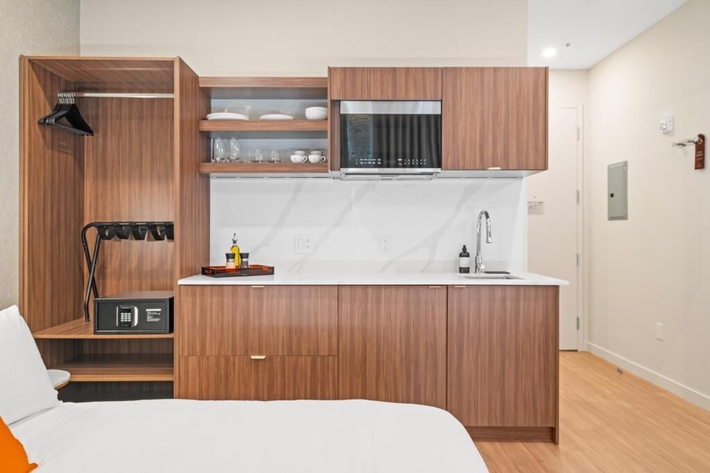 A compact hotel room with a kitchenette, a bed, and a small seating area.