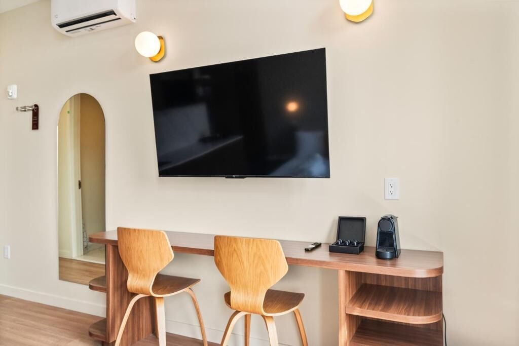 Habitación moderna con una televisión de pantalla plana montada en la pared, dos sillas de madera, una mesita pequeña de madera y una estantería empotrada.