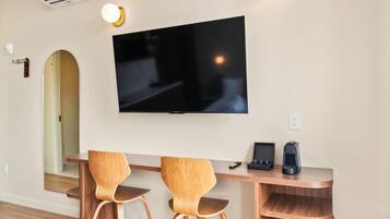 Habitación moderna con una televisión de pantalla plana montada en la pared, dos sillas de madera, una mesita pequeña de madera y una estantería empotrada.