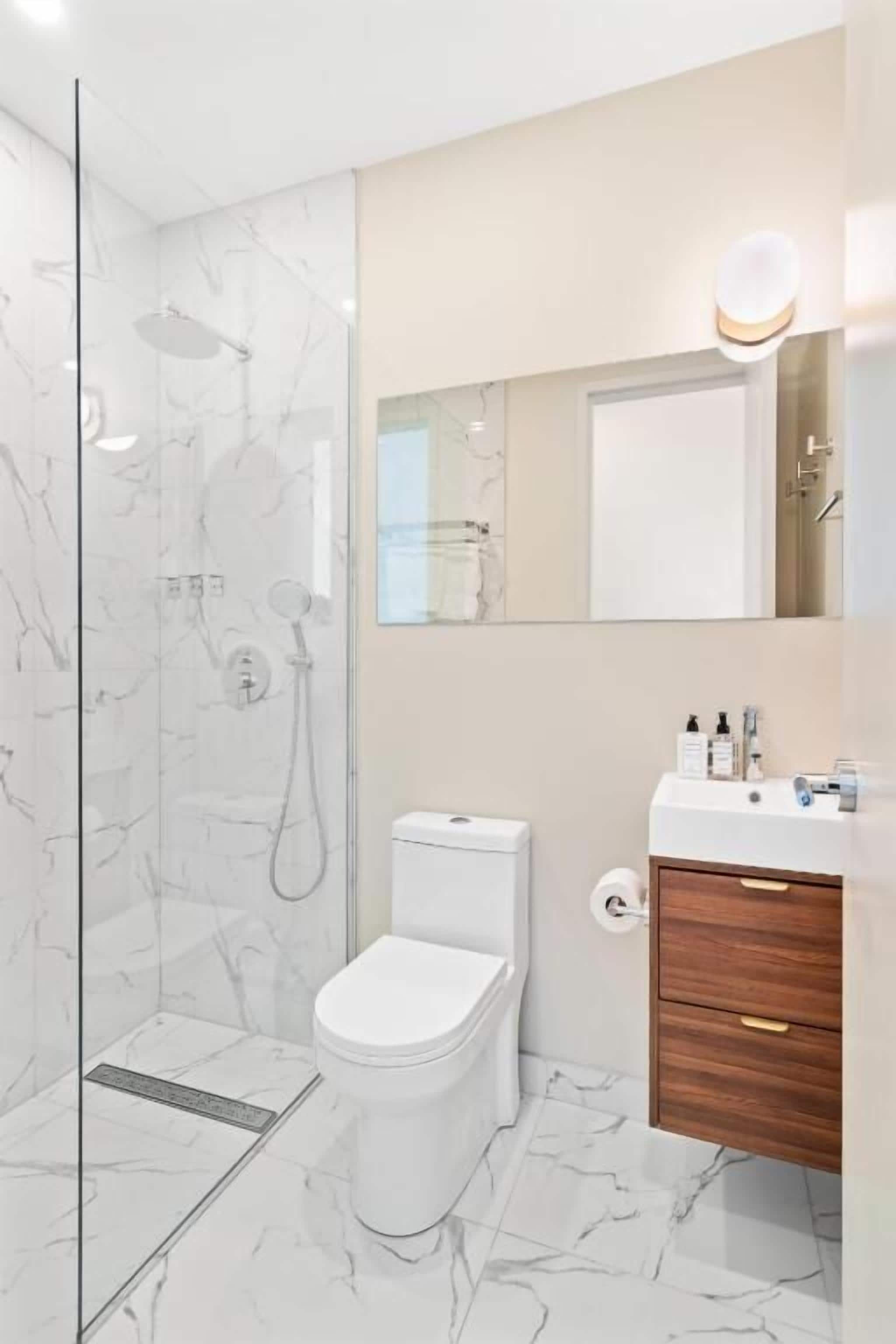 A modern bathroom with a glass-enclosed shower, a white toilet, and a wooden vanity with a mirror.