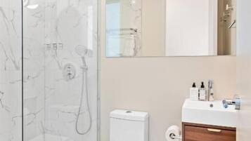 A modern bathroom with a glass-enclosed shower, a white toilet, and a wooden vanity with a mirror.