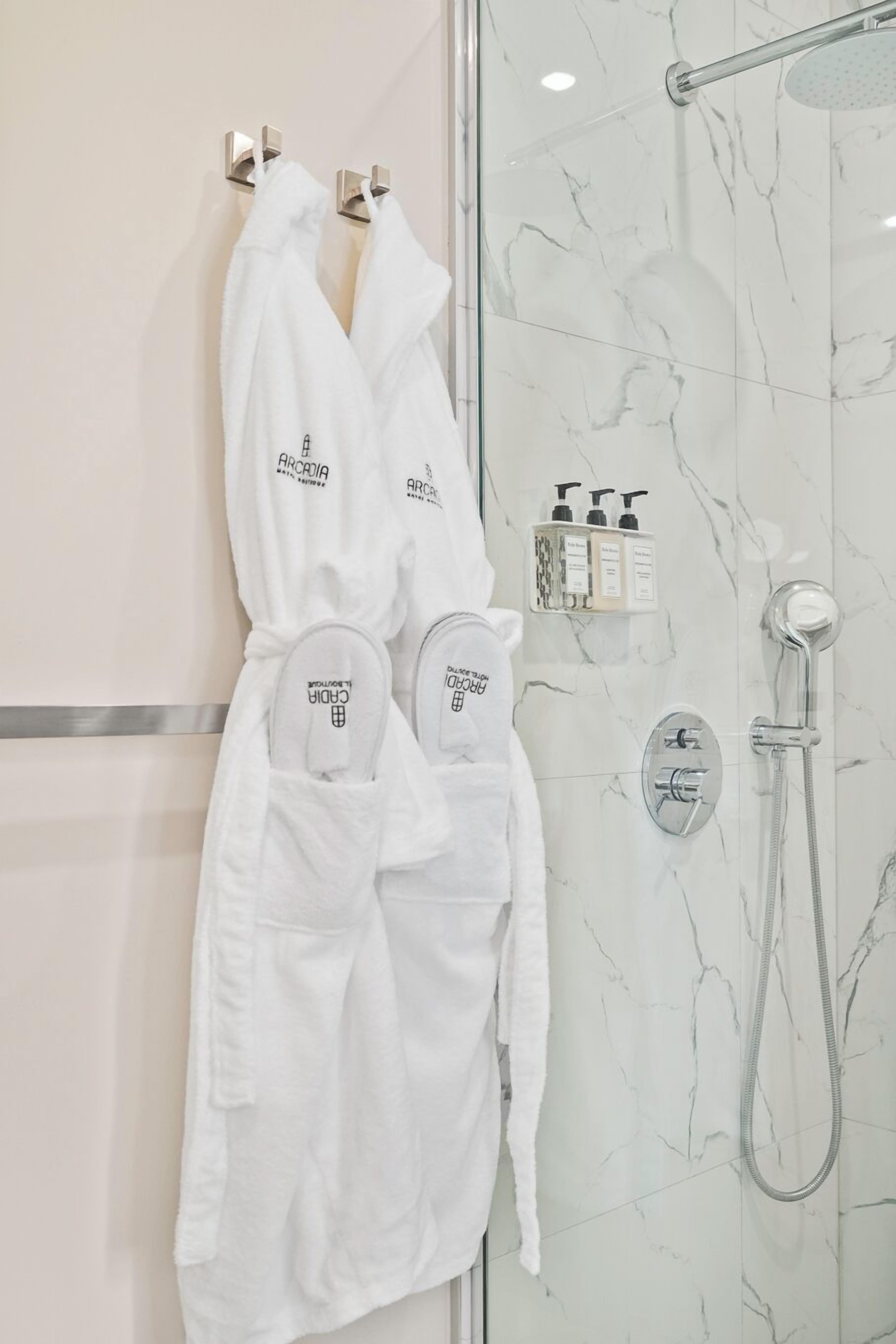 Une salle de bain dotée d’une douche à parois de verre, d’un mur en marbre et de deux peignoirs blancs suspendus à un porte-serviettes.
