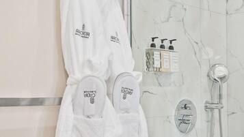 Une salle de bain dotée d’une douche à parois de verre, d’un mur en marbre et de deux peignoirs blancs suspendus à un porte-serviettes.