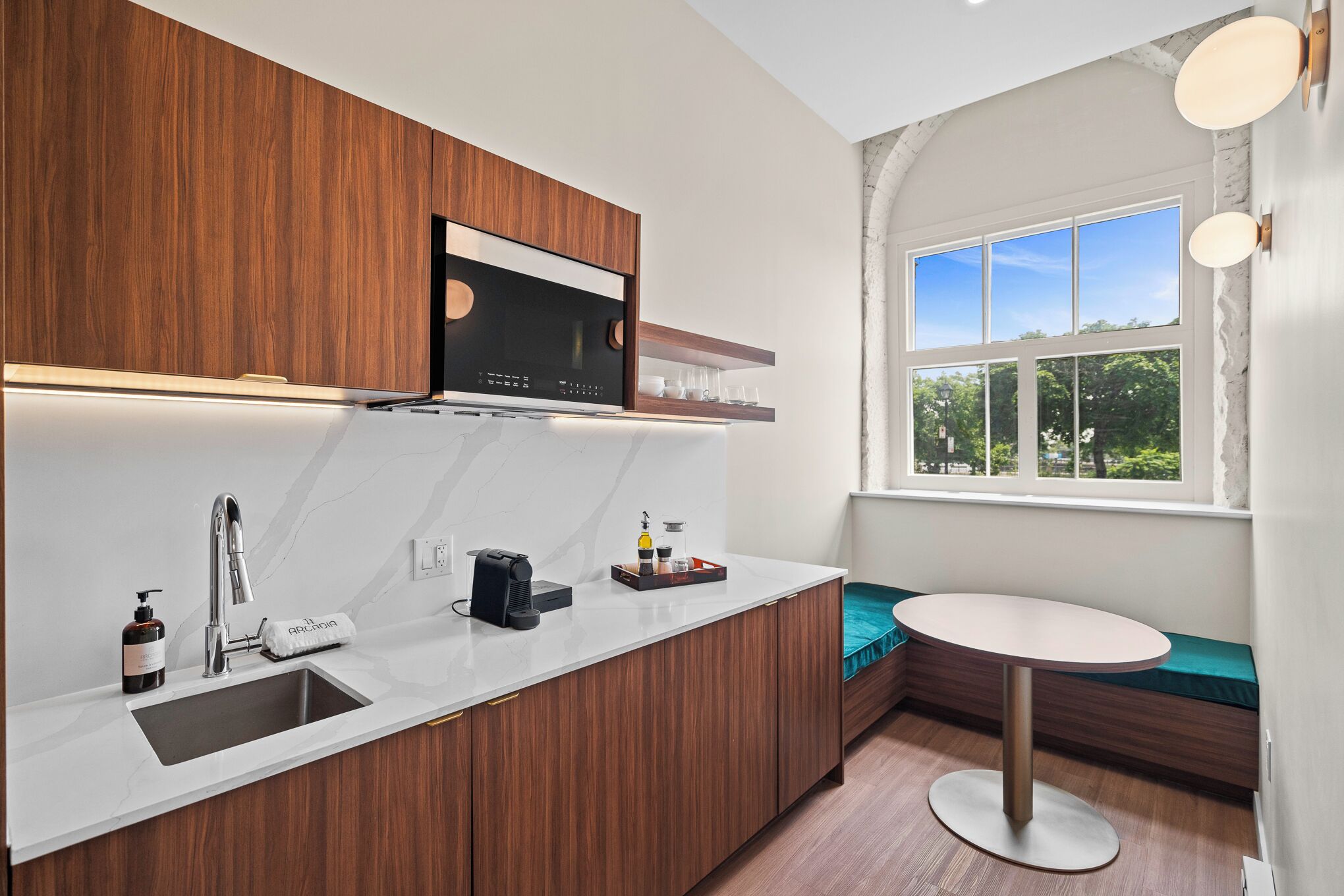 A modern kitchen with a built-in microwave, a sink, and a coffee maker. There is a window with a view of greenery outside.
