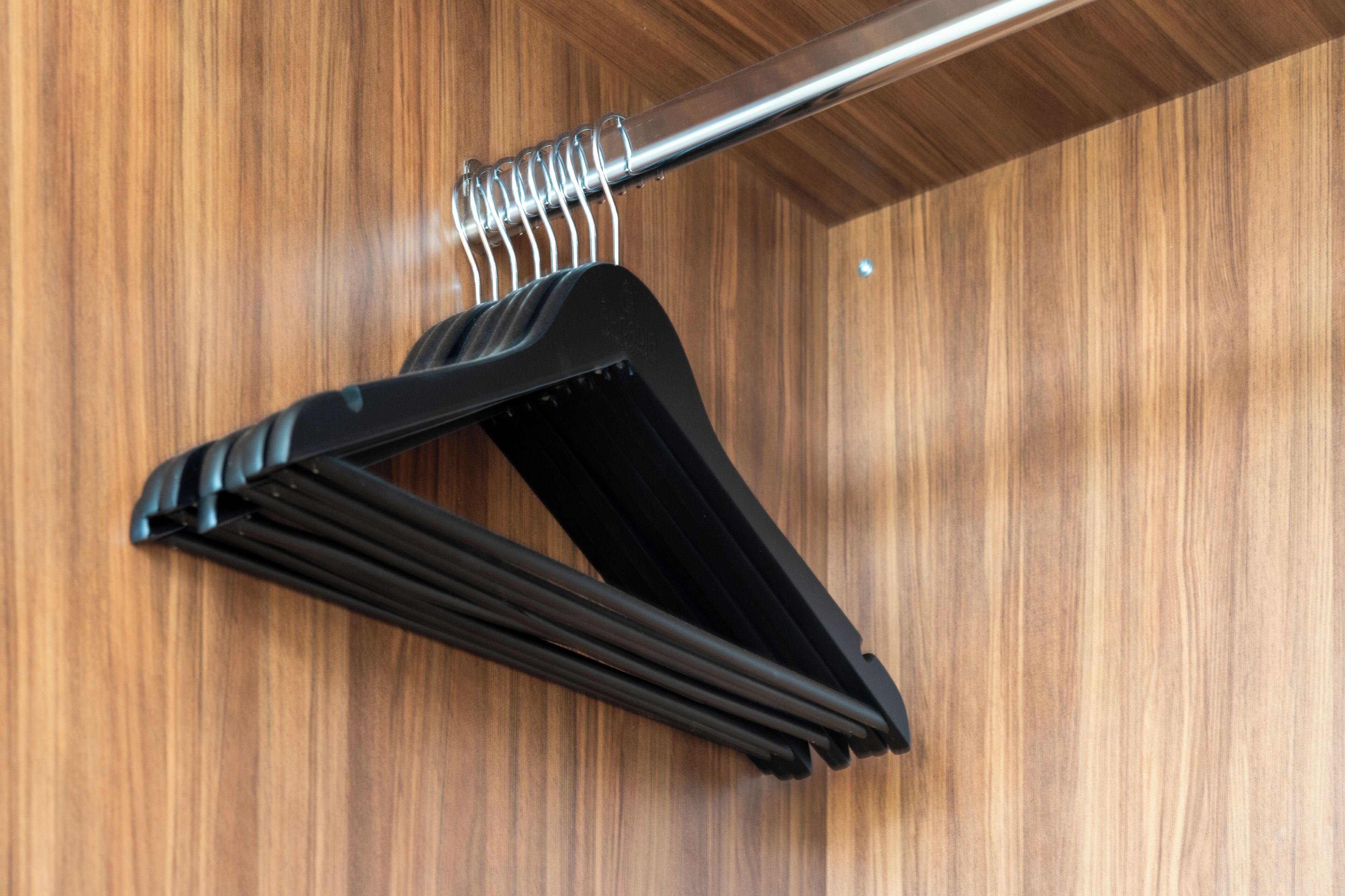 Un armario de madera con una barra metálica y un perchero negro.