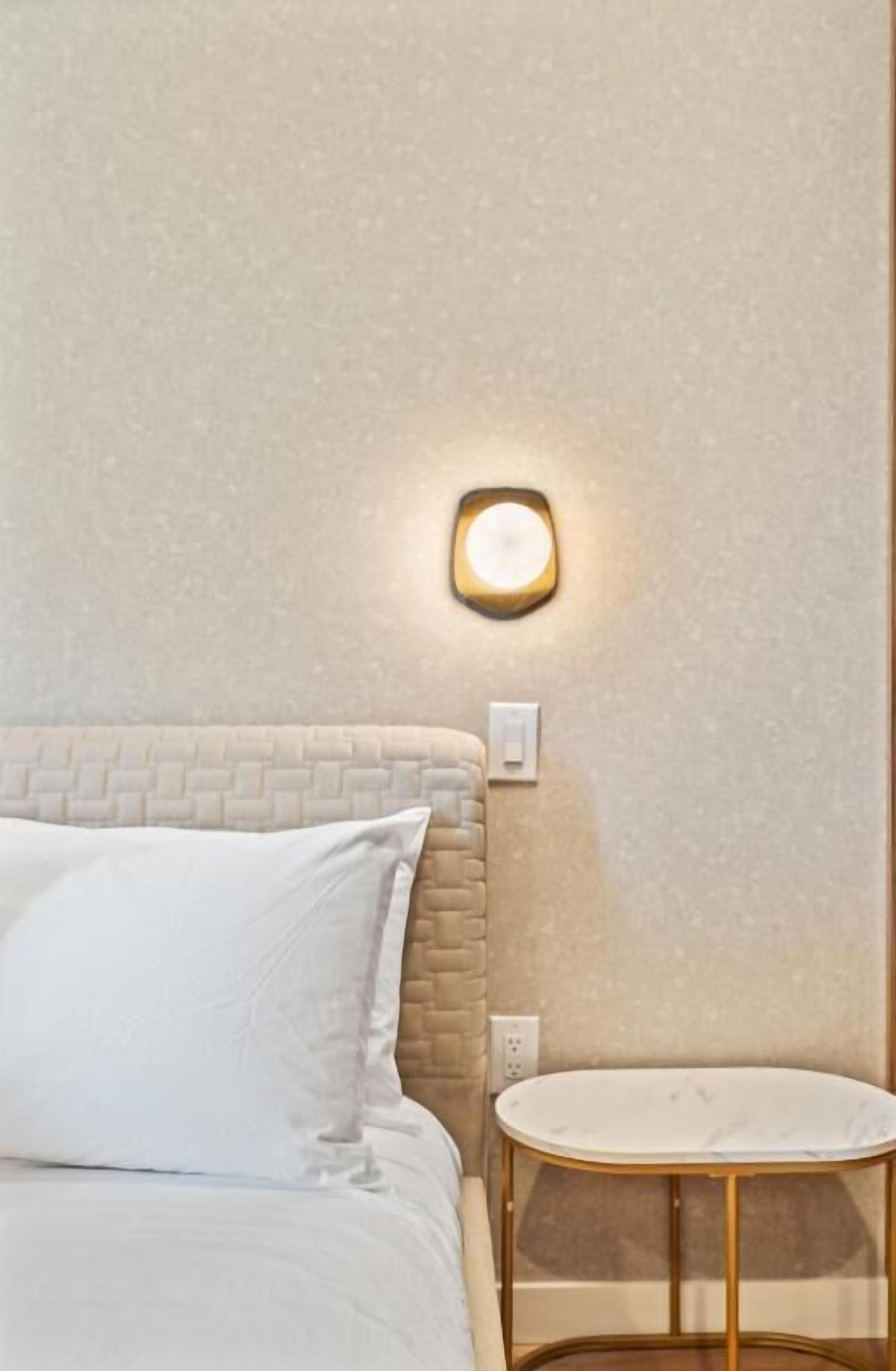 A bed with a headboard, a bedside table, and a wall-mounted light fixture.
