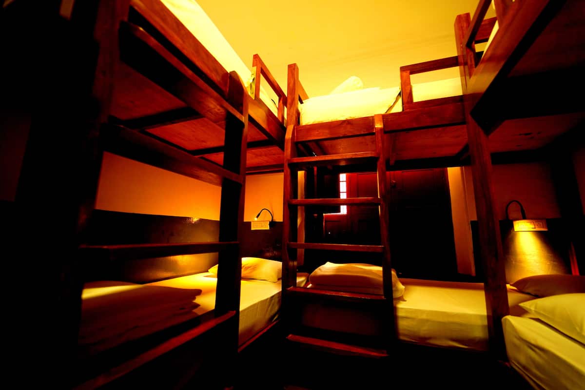 Une chambre avec des lits superposés en bois, une table de chevet et une lampe fixée au mur.