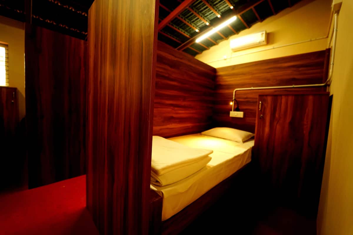 Une pièce de taille modeste, meublée en bois, comprenant un lit simple, une table de chevet et un luminaire fixé au mur.