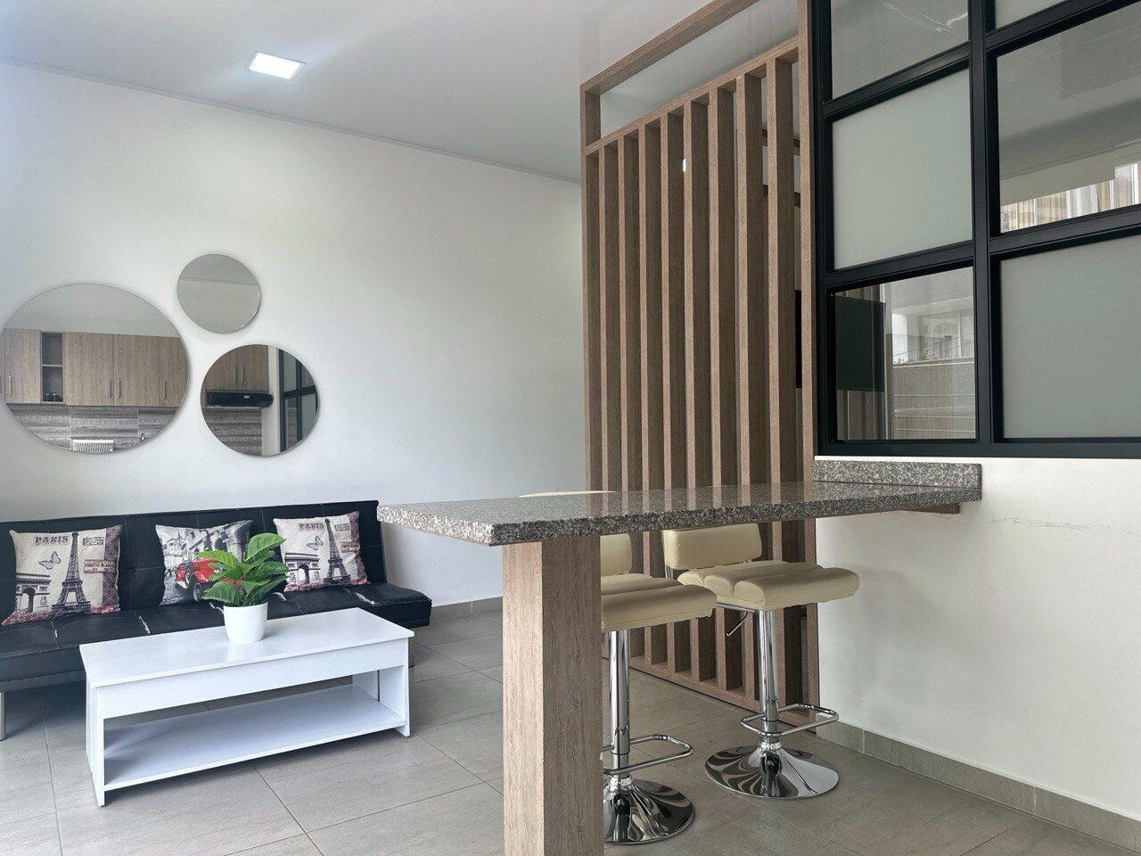Un salon moderne avec un canapé blanc, une table basse et un coin bar équipé de tabourets.