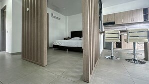 Une chambre d’hôtel moderne équipée d’un lit, d’une kitchenette et d’un coin salon avec des tabourets de bar.