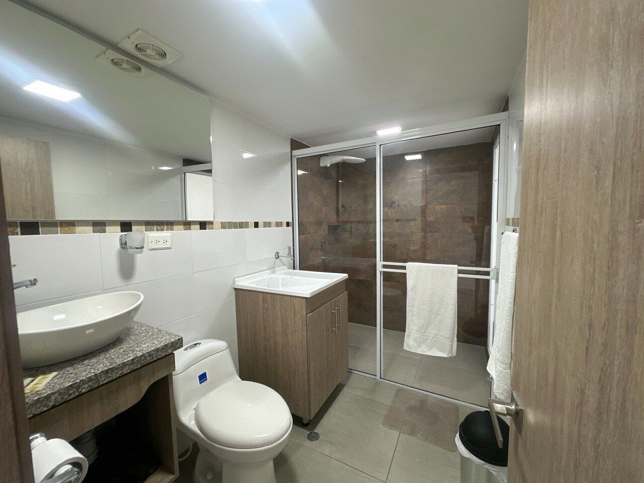 A modern bathroom with a large sink, toilet, and a glass shower enclosure.