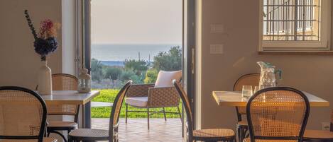 A dining area with a view of the sea, featuring wicker chairs and a table with a vase of flowers.