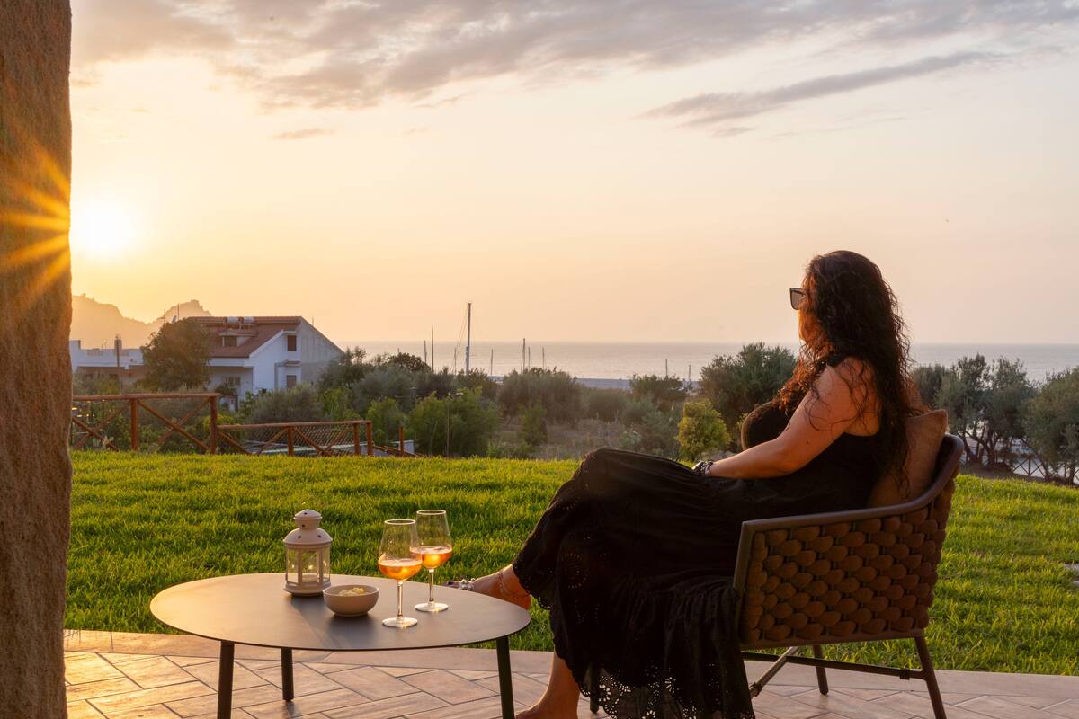 Una mujer sentada en una silla a una mesa, con vista al mar y al atardecer.