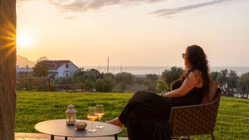 Una mujer sentada en una silla a una mesa, con vista al mar y al atardecer.