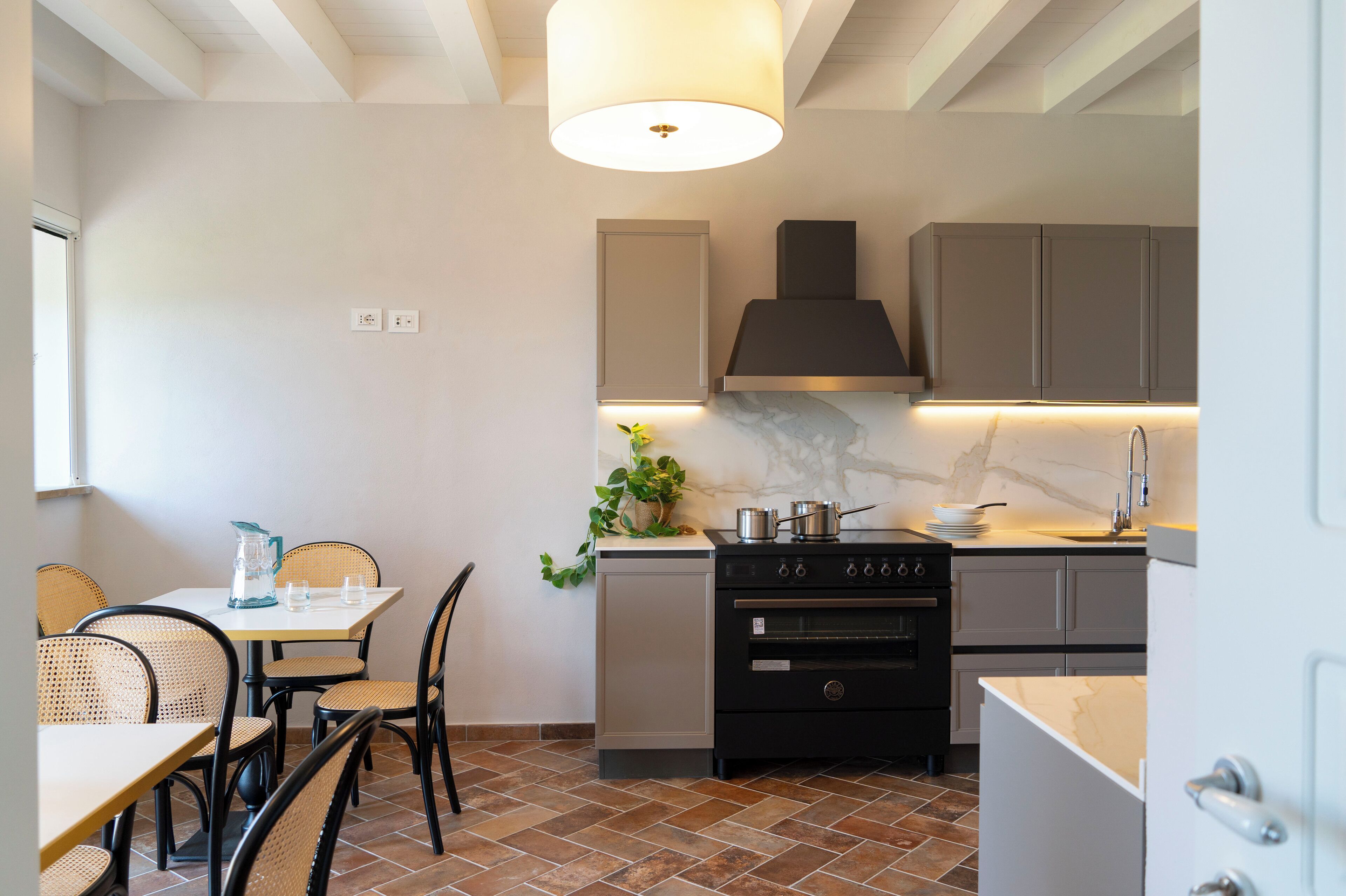 A compact kitchen with a built-in oven, a stove, and a sink. There is a dining table with chairs and a hanging light fixture above it.