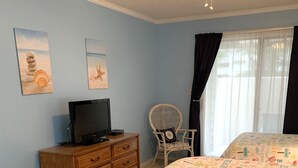 A bedroom with a bed, a wooden dresser, a television, a wicker chair, and two wall art pieces. - Beach Retreat 3BR Ground Floor Condo in Kingston Plantation! (Myrtle Beach)