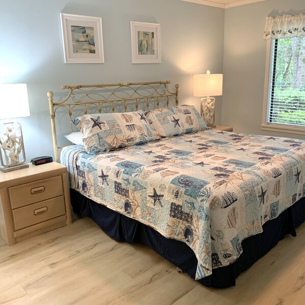 Un dormitorio con cama, mesitas de noche, lámpara y cuadros en la pared.