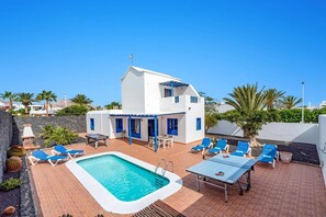 Un edificio blanco con detalles azules, piscina y mobiliario exterior.