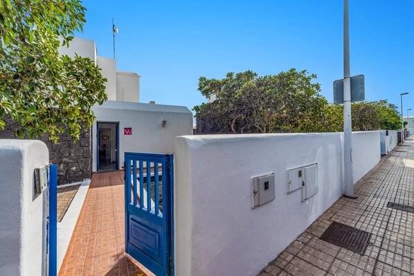 Un edificio de paredes blancas con una verja azul, un muro de piedra y un sendero pavimentado.