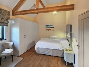 Un dormitorio con una cama, una silla, un armario, un radiador y un cuadro en la pared.