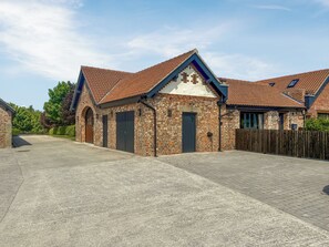 A brick building with a tiled roof, a paved driveway, and a wooden fence.